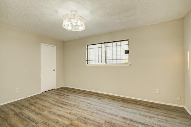 unfurnished room with baseboards, wood finished floors, an inviting chandelier, and a textured ceiling
