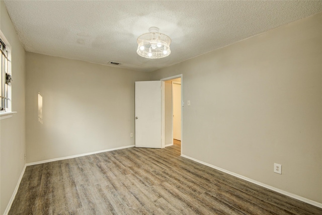 unfurnished room featuring wood finished floors, baseboards, visible vents, a notable chandelier, and a textured ceiling