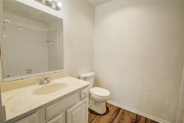 bathroom with wood finished floors, walk in shower, toilet, a textured wall, and vanity