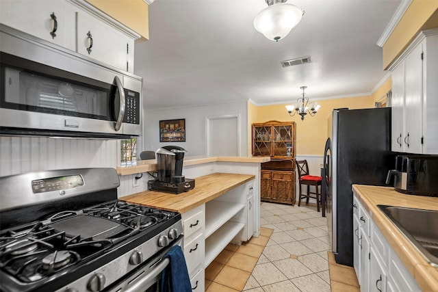 kitchen featuring butcher block countertops, a chandelier, light tile patterned floors, stainless steel appliances, and ornamental molding