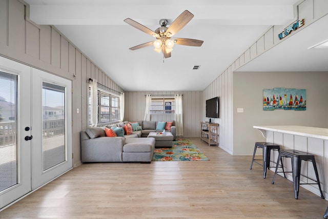 living area featuring lofted ceiling with beams, a ceiling fan, visible vents, and light wood finished floors