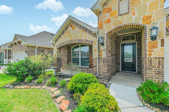 view of exterior entry with brick siding, roof with shingles, stone siding, and a garage