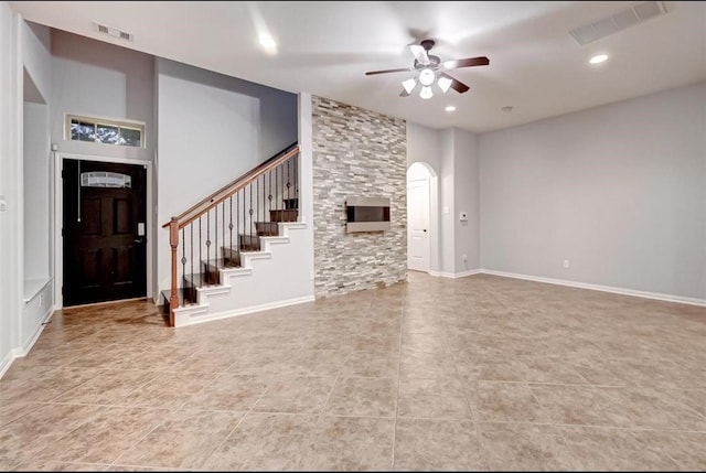 unfurnished living room featuring a ceiling fan, visible vents, arched walkways, and stairway