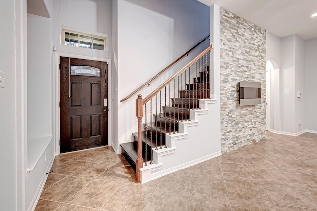 entryway featuring arched walkways, a towering ceiling, stairs, and tile patterned floors
