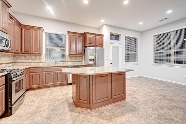 kitchen featuring a center island, a sink, tasteful backsplash, light stone counters, and appliances with stainless steel finishes