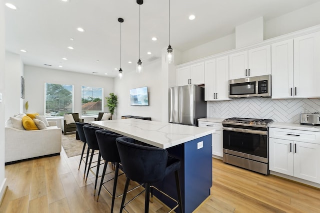 kitchen featuring open floor plan, backsplash, white cabinetry, a kitchen island, and appliances with stainless steel finishes