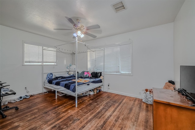 bedroom with baseboards, hardwood / wood-style flooring, visible vents, and a ceiling fan
