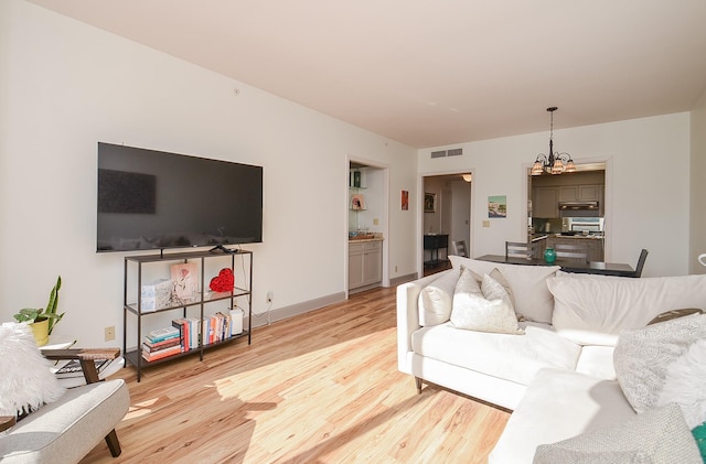 living area featuring baseboards, light wood-style flooring, visible vents, and a chandelier