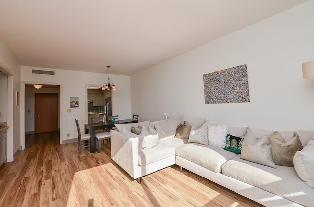 living area featuring light wood-type flooring, visible vents, and a notable chandelier