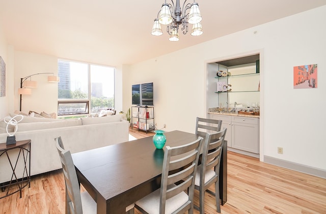 dining area featuring light wood finished floors, an inviting chandelier, and wet bar