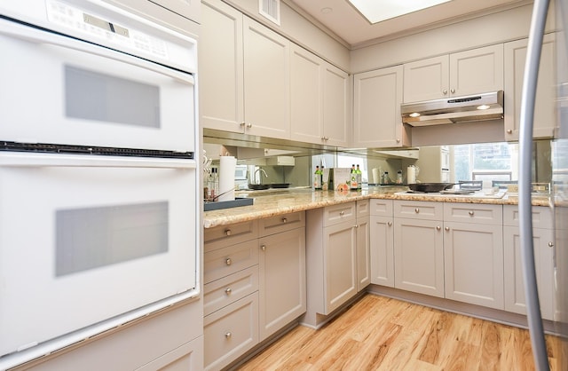 kitchen with visible vents, under cabinet range hood, light wood-style floors, and white appliances