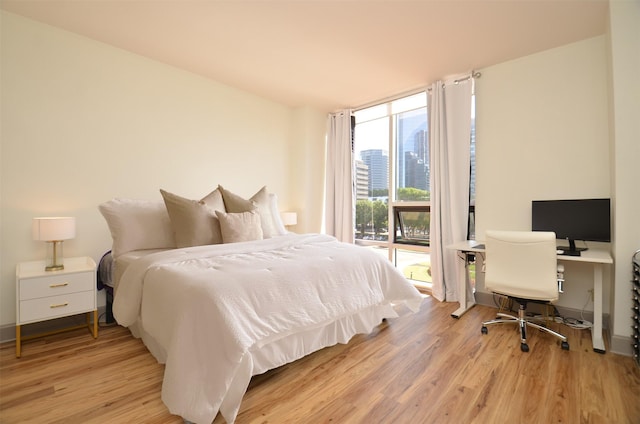 bedroom with a wall of windows, baseboards, and light wood-style floors