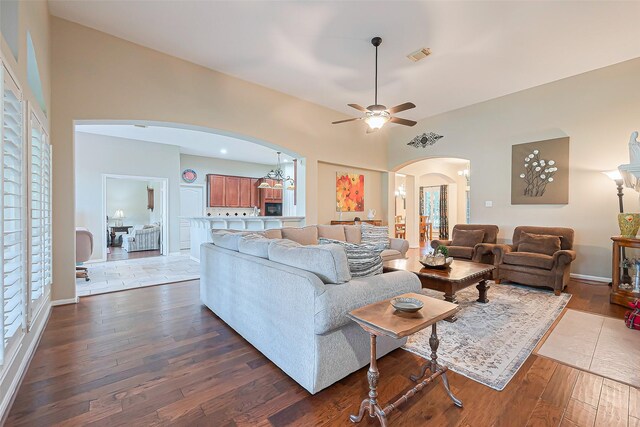 living room featuring arched walkways, dark wood-style flooring, baseboards, visible vents, and ceiling fan