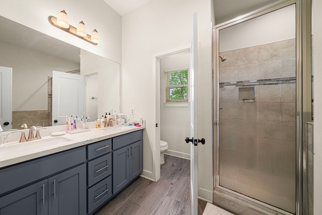 bathroom featuring a sink, double vanity, toilet, wood finished floors, and a shower stall