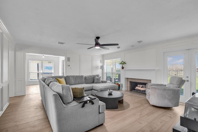 living area featuring visible vents, a decorative wall, plenty of natural light, a tile fireplace, and light wood finished floors