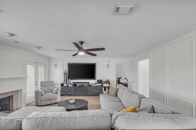 living room featuring ceiling fan, a decorative wall, wood finished floors, and visible vents