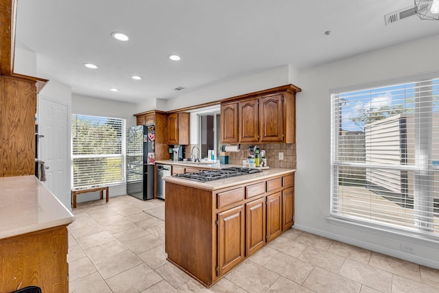 kitchen with gas cooktop, dishwasher, light countertops, freestanding refrigerator, and a peninsula