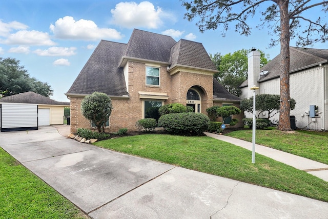 view of front of house with roof with shingles, a front lawn, brick siding, a detached garage, and an outdoor structure