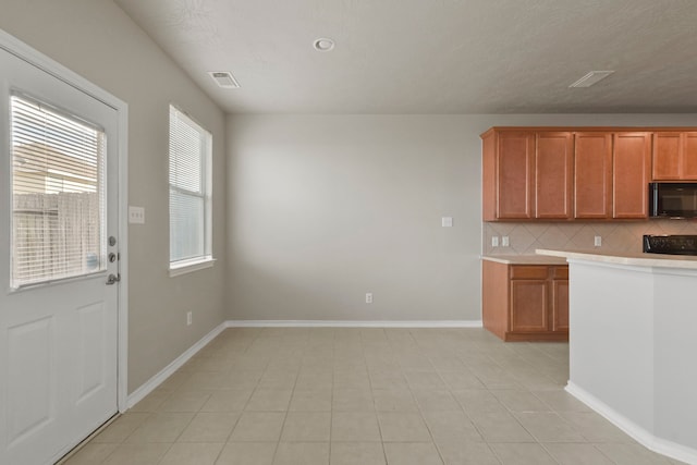 kitchen featuring decorative backsplash, black microwave, light countertops, baseboards, and visible vents