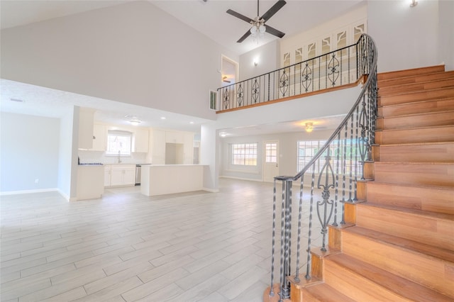 stairway with a ceiling fan, baseboards, a high ceiling, and wood finished floors