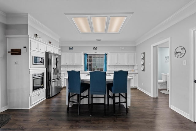 kitchen with a kitchen bar, white cabinets, light countertops, appliances with stainless steel finishes, and decorative backsplash