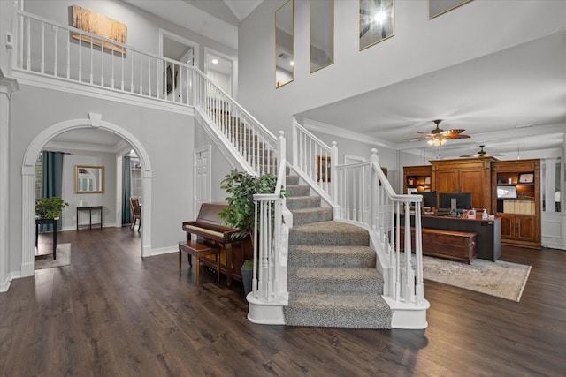 stairway with wood finished floors, a towering ceiling, arched walkways, a ceiling fan, and baseboards