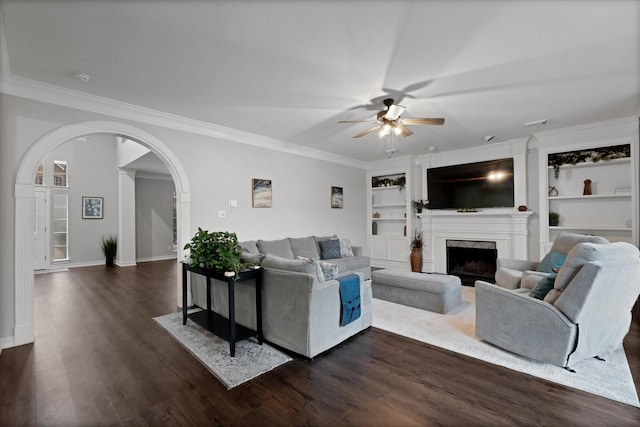 living area with crown molding, dark wood-type flooring, a fireplace, and a ceiling fan