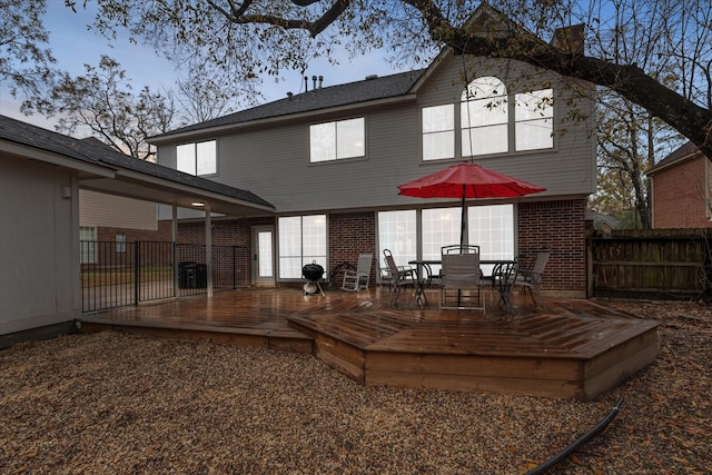 back of property with fence, a deck, outdoor dining area, and brick siding