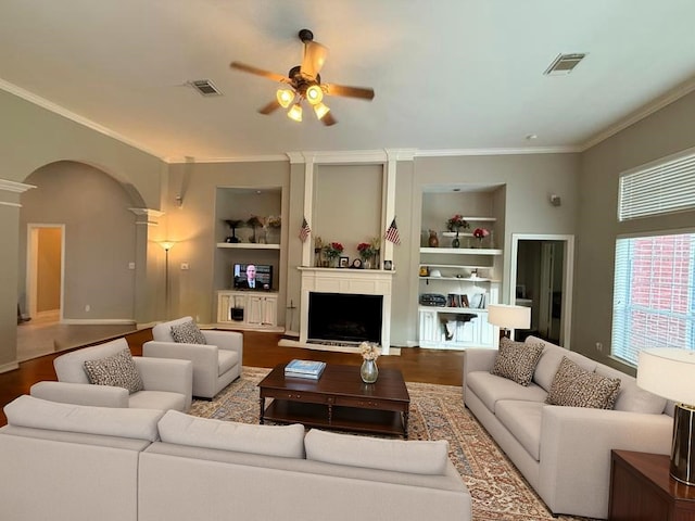 living area with visible vents, crown molding, ceiling fan, built in shelves, and arched walkways