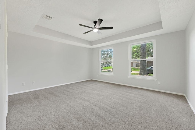 carpeted empty room featuring a ceiling fan, a textured ceiling, a raised ceiling, baseboards, and visible vents