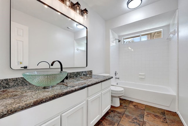 full bathroom with stone tile floors, vanity, washtub / shower combination, baseboards, and toilet
