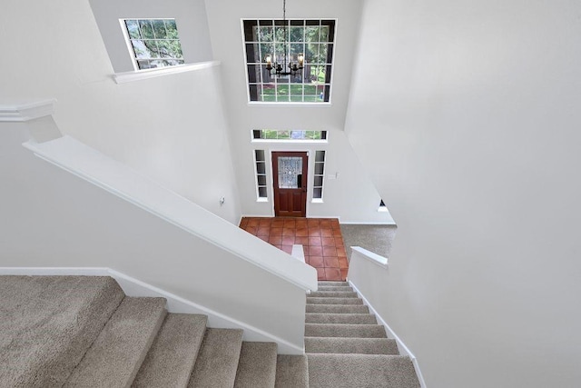 stairs featuring tile patterned floors, baseboards, a towering ceiling, carpet, and a notable chandelier