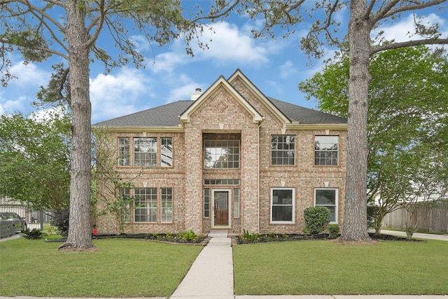 view of front of house featuring brick siding, a chimney, a front yard, and fence