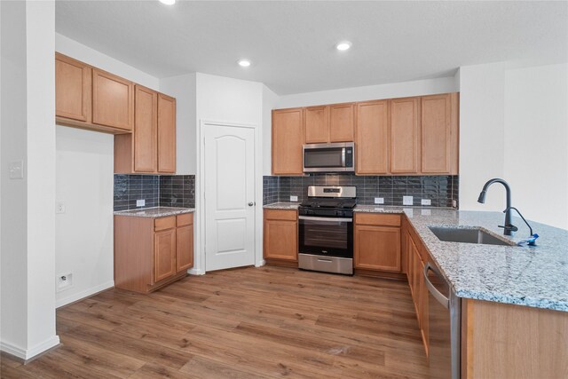 kitchen featuring a sink, decorative backsplash, light wood-type flooring, appliances with stainless steel finishes, and light stone countertops