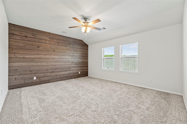 carpeted spare room featuring vaulted ceiling, visible vents, baseboards, ceiling fan, and wooden walls