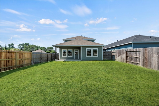 rear view of property featuring a lawn, roof with shingles, a patio, and a fenced backyard