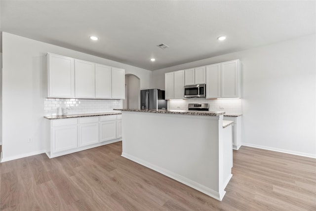 kitchen with light wood finished floors, backsplash, visible vents, arched walkways, and appliances with stainless steel finishes
