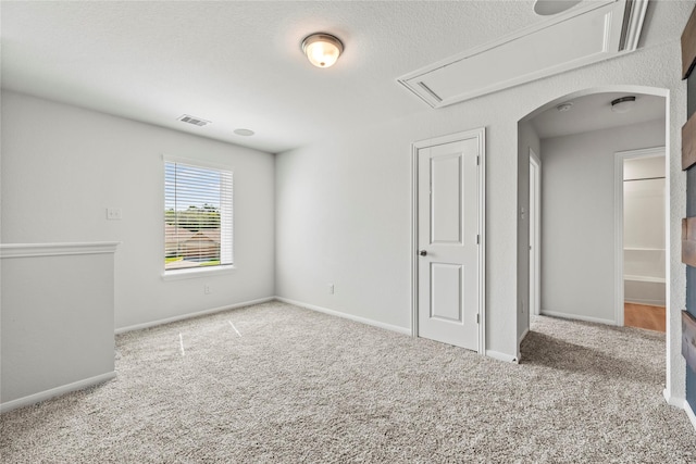 carpeted empty room with baseboards, visible vents, arched walkways, and a textured ceiling