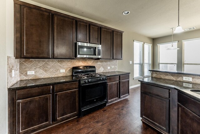 3713 Daisy Ln, Huntsville, TX 77340 - kitchen with dark stone countertops, stainless steel microwave, dark wood finished floors, dark brown cabinetry, and black range with gas cooktop