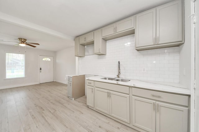 kitchen with ceiling fan, a sink, light wood finished floors, baseboards, and decorative backsplash