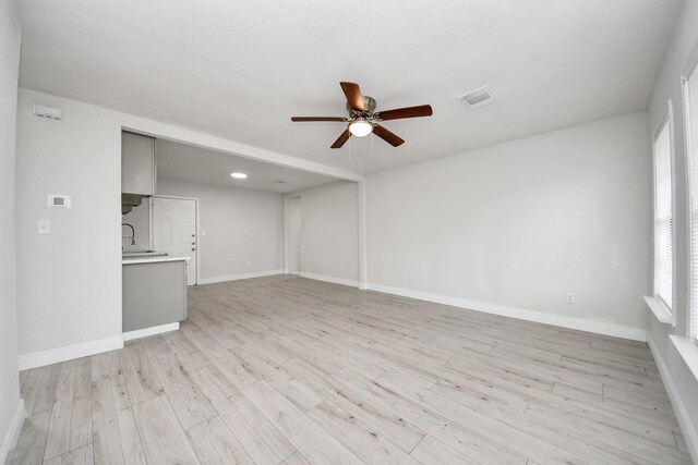 unfurnished living room with baseboards, a ceiling fan, and light wood-type flooring