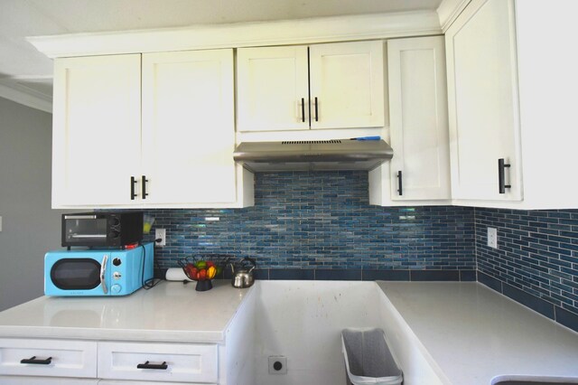 504 Cedar St, Sweeny, TX 77480 - kitchen with under cabinet range hood, tasteful backsplash, white cabinetry, light countertops, and ornamental molding