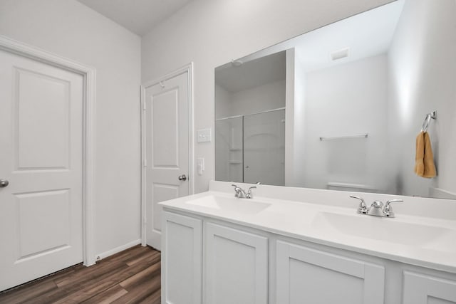 bathroom featuring an enclosed shower, wood finished floors, a sink, and double vanity