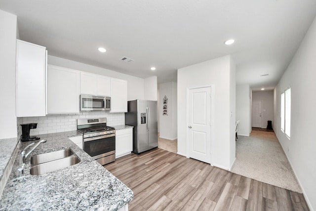 kitchen with decorative backsplash, white cabinetry, light wood-style flooring, appliances with stainless steel finishes, and visible vents