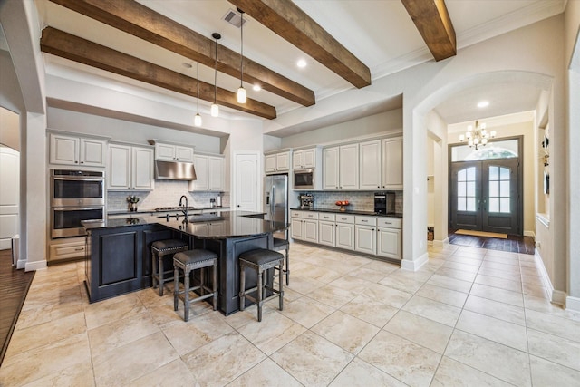 8207 Mesquite Hill Ln, Richmond, TX 77469 - kitchen featuring decorative backsplash, beam ceiling, under cabinet range hood, arched walkways, and stainless steel appliances