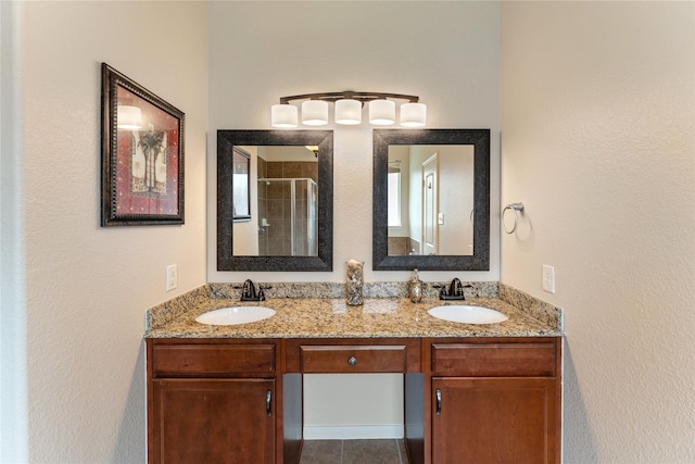 full bathroom with a shower stall, a textured wall, double vanity, and a sink