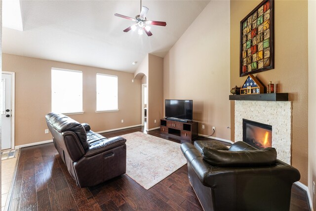 living room with dark wood-style floors, arched walkways, vaulted ceiling, ceiling fan, and a fireplace