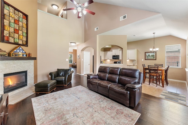 living room with ceiling fan with notable chandelier, visible vents, a fireplace, and dark wood-style floors