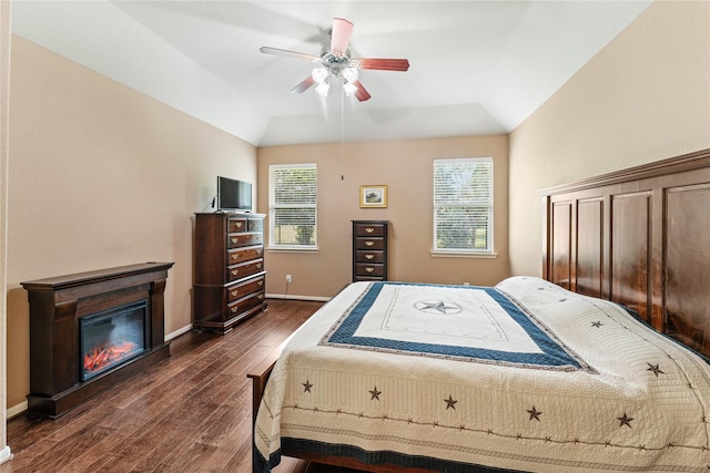 bedroom with dark wood finished floors, baseboards, a glass covered fireplace, lofted ceiling, and a ceiling fan