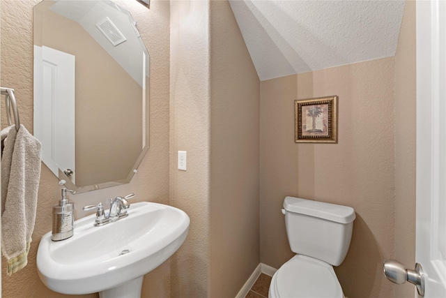 bathroom featuring vaulted ceiling, a textured ceiling, toilet, and a sink